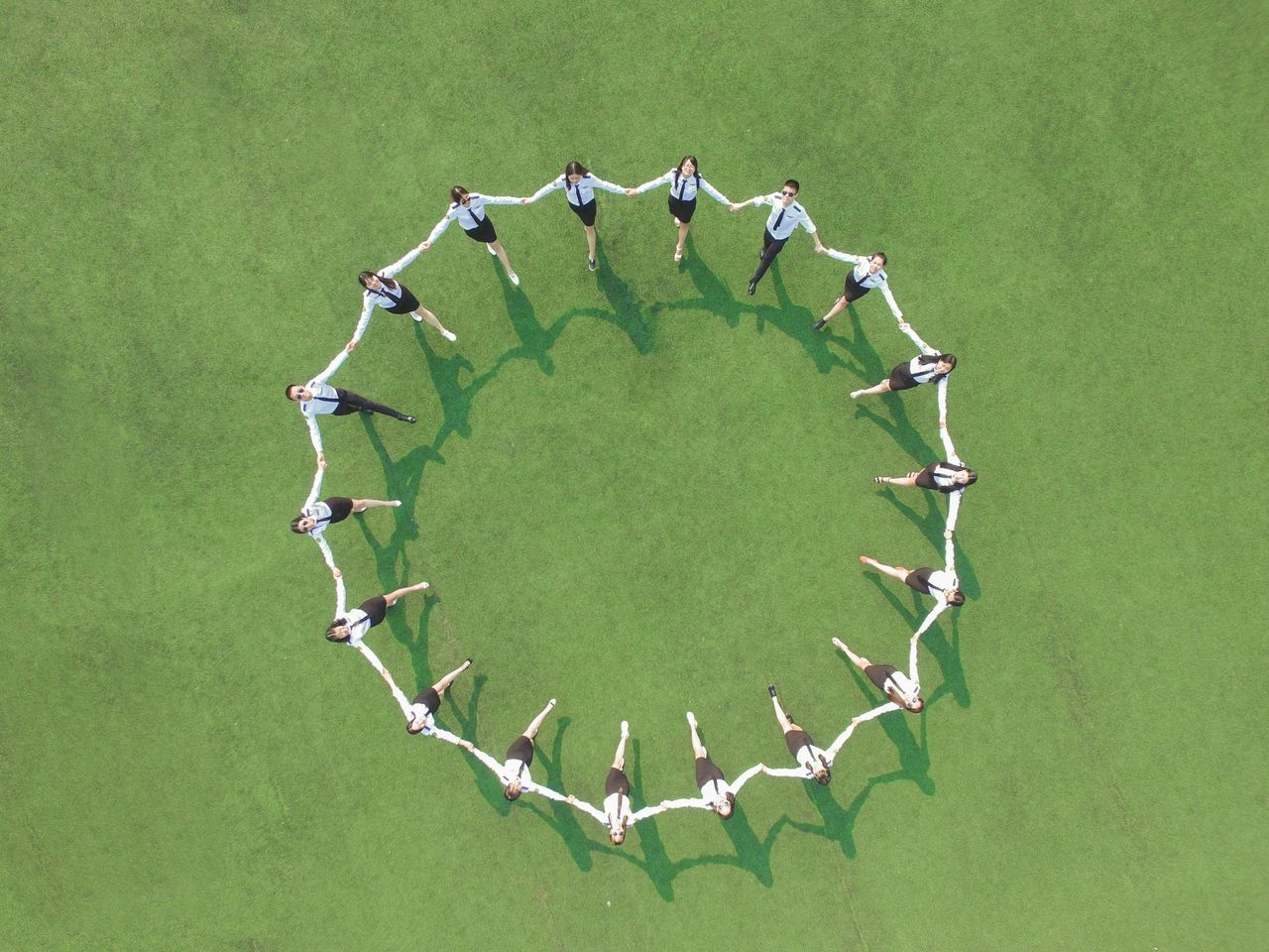 Home Aerial shot of a group forming a circle on a green field, holding hands and connected.